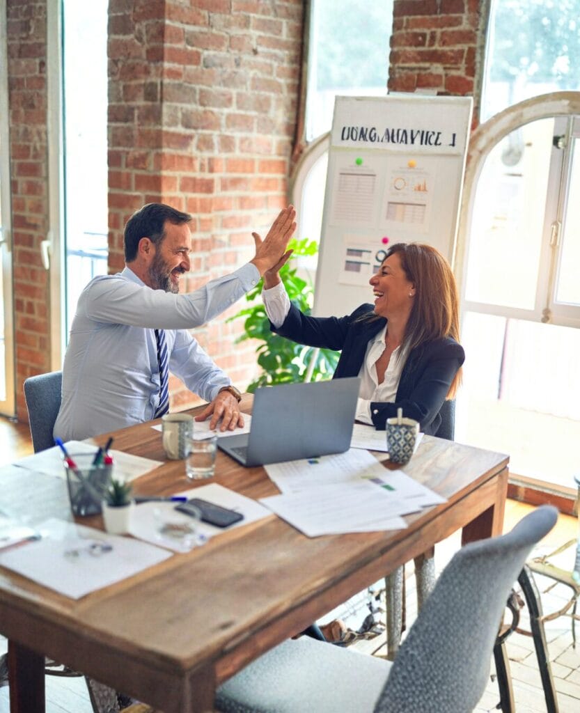 Two colleagues high-fiving in a modern office workspace, demonstrating behavioral intelligence through effective workplace communication and collaboration