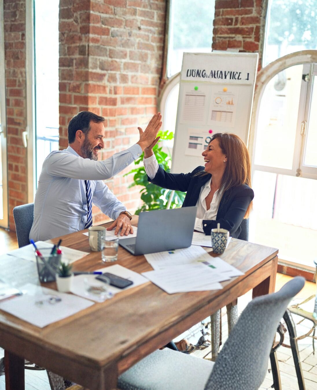 Two colleagues high-fiving in a modern office workspace, demonstrating behavioral intelligence through effective workplace communication and collaboration