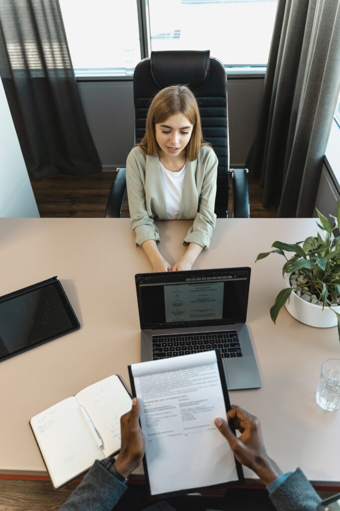 A candidate talks with a hiring manager across a desk during a final-stage interview, with notes and a document on the table.